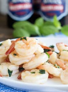 White plate with cooked shrimp with bits of basil.