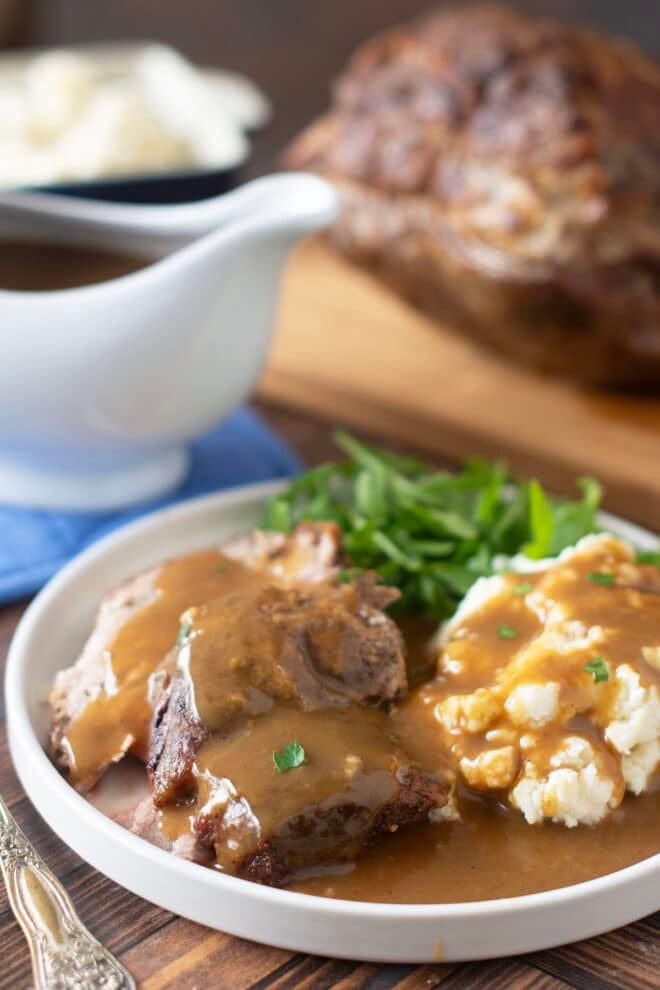 Homemade pork gravy over slices of pork and mashed potatoes on a plate with greens.