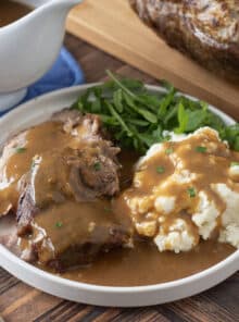 Homemade pork gravy over slices of pork and mashed potatoes on a plate with greens.