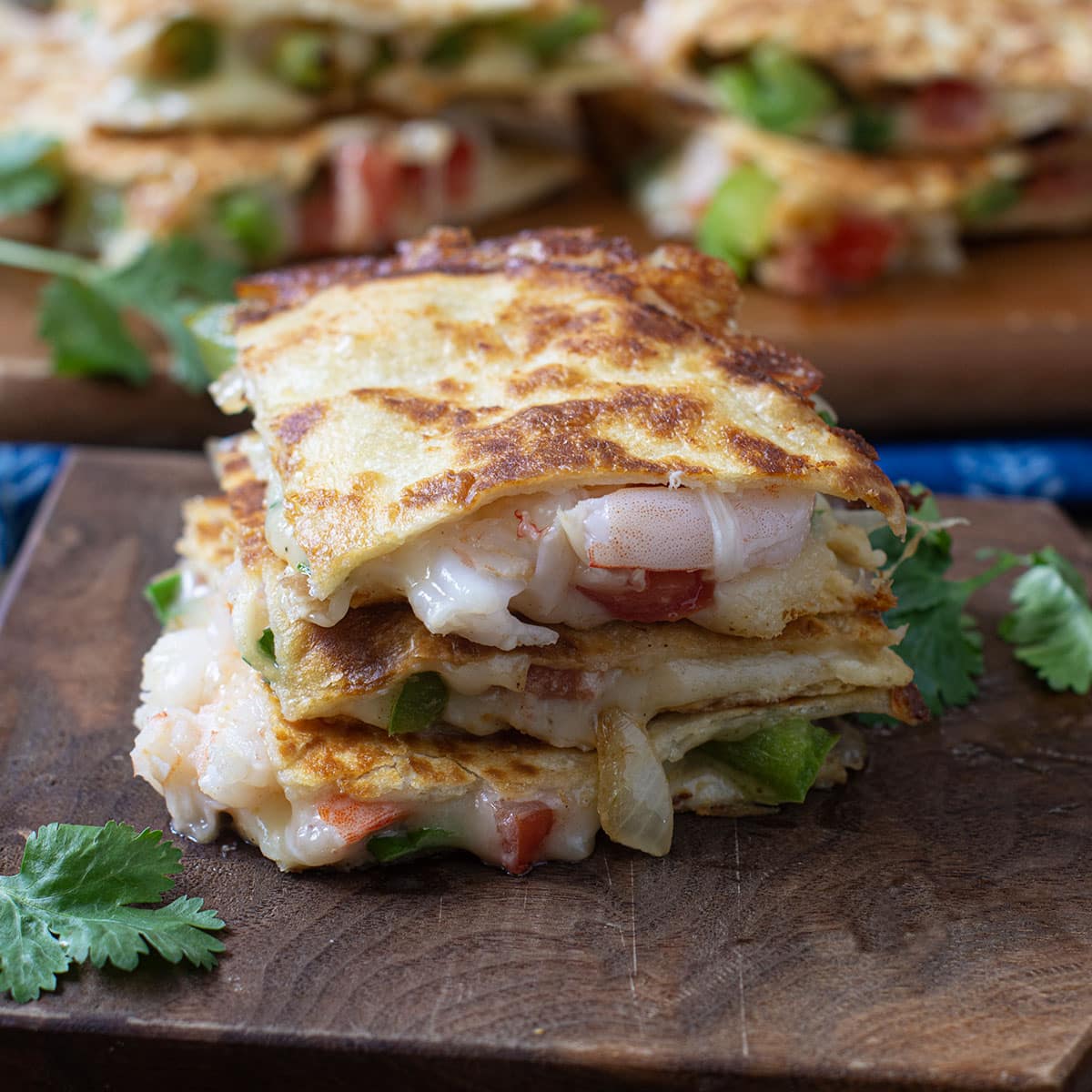 Wedges of shrimp quesadilla stacked on a wooden cutting board.