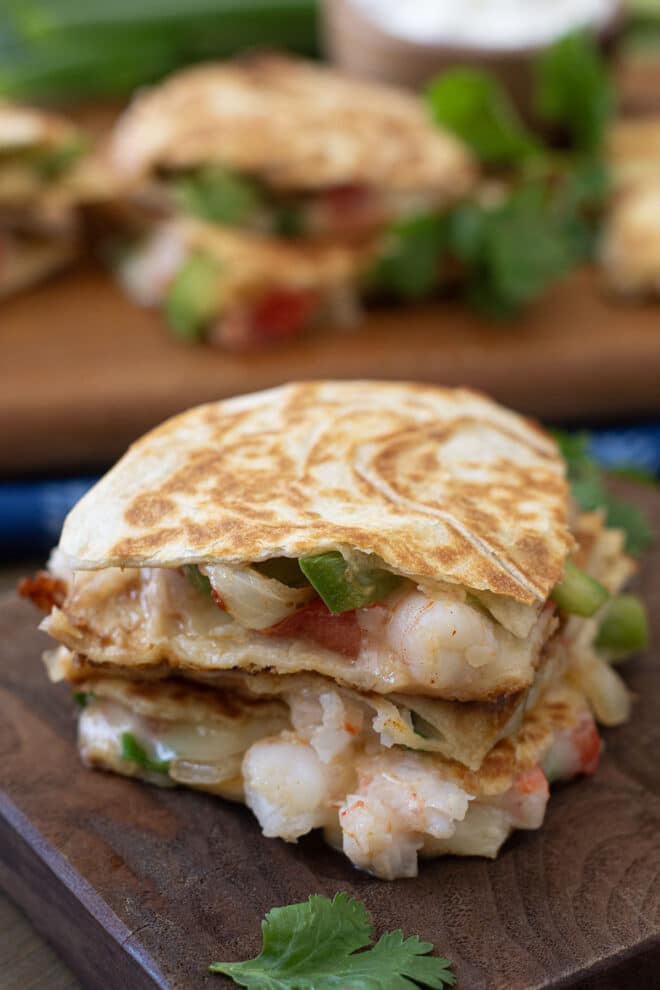 Wedges of shrimp quesadilla stacked on a wooden cutting board.