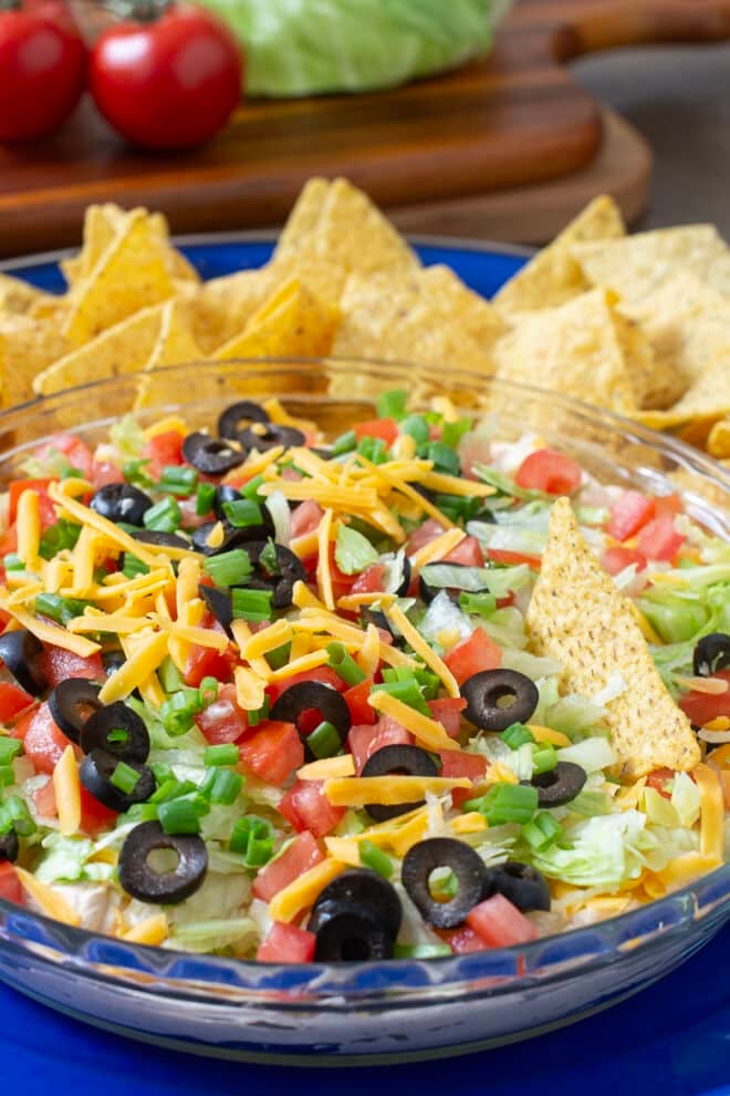 Classic Taco Dip with cheese, olives, lettuce, and tomato with tortilla chips in background.