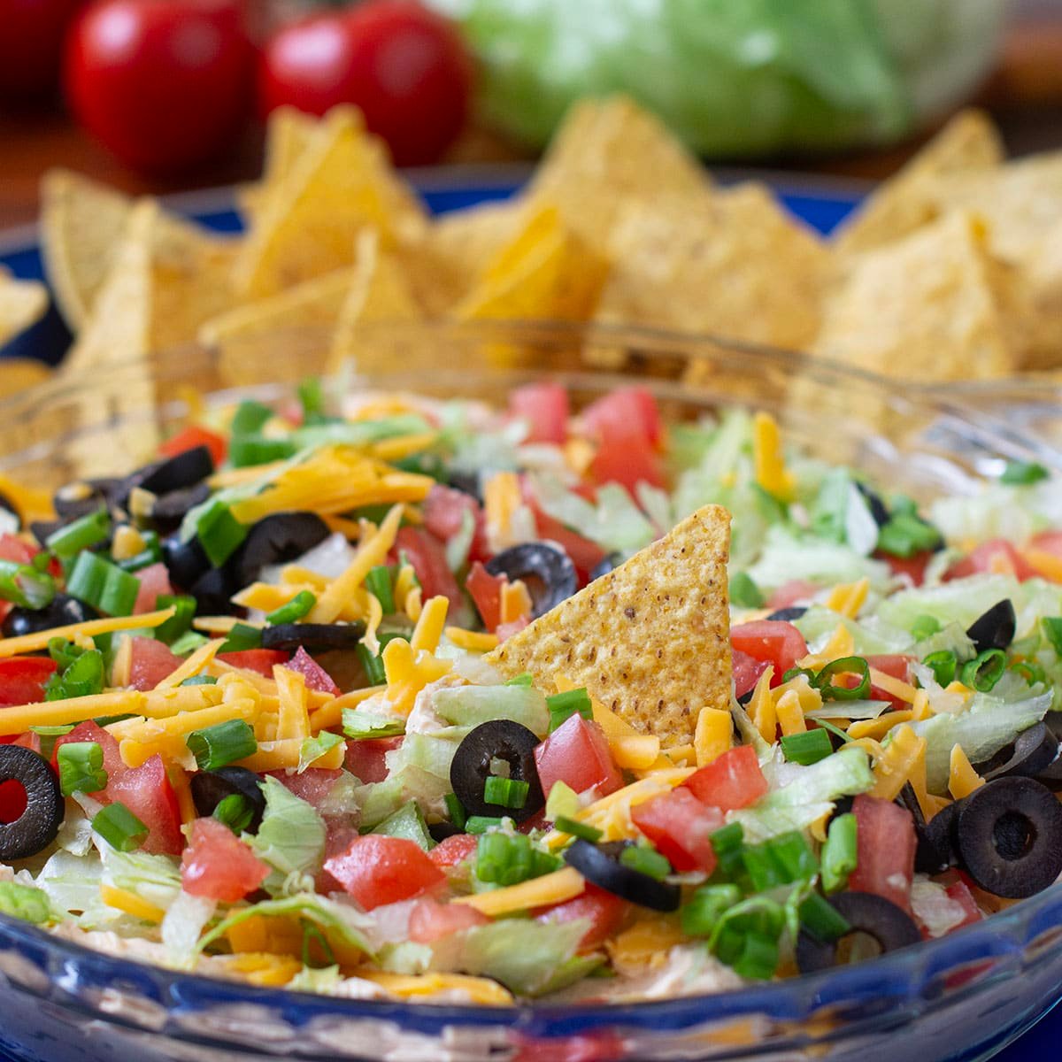 Classic Taco Dip with cheese, olives, lettuce, and tomato with tortilla chips in background.