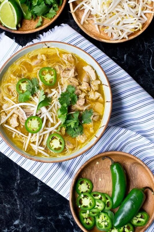 Bowl of turkey pho soup with dishes of lime, bean sprouts, and jalapenos around.