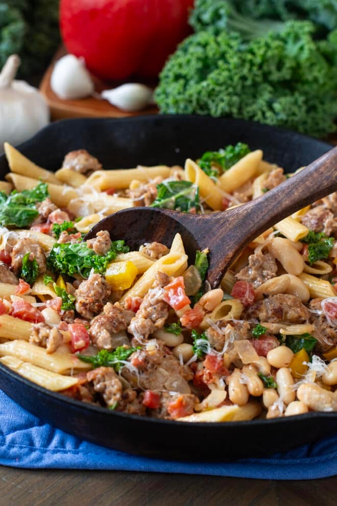 Skillet of pasta with sausage, tomato, kale, and cheese.