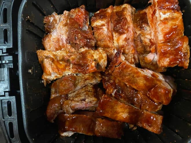 cut up cooked ribs in air fryer basket with sauce