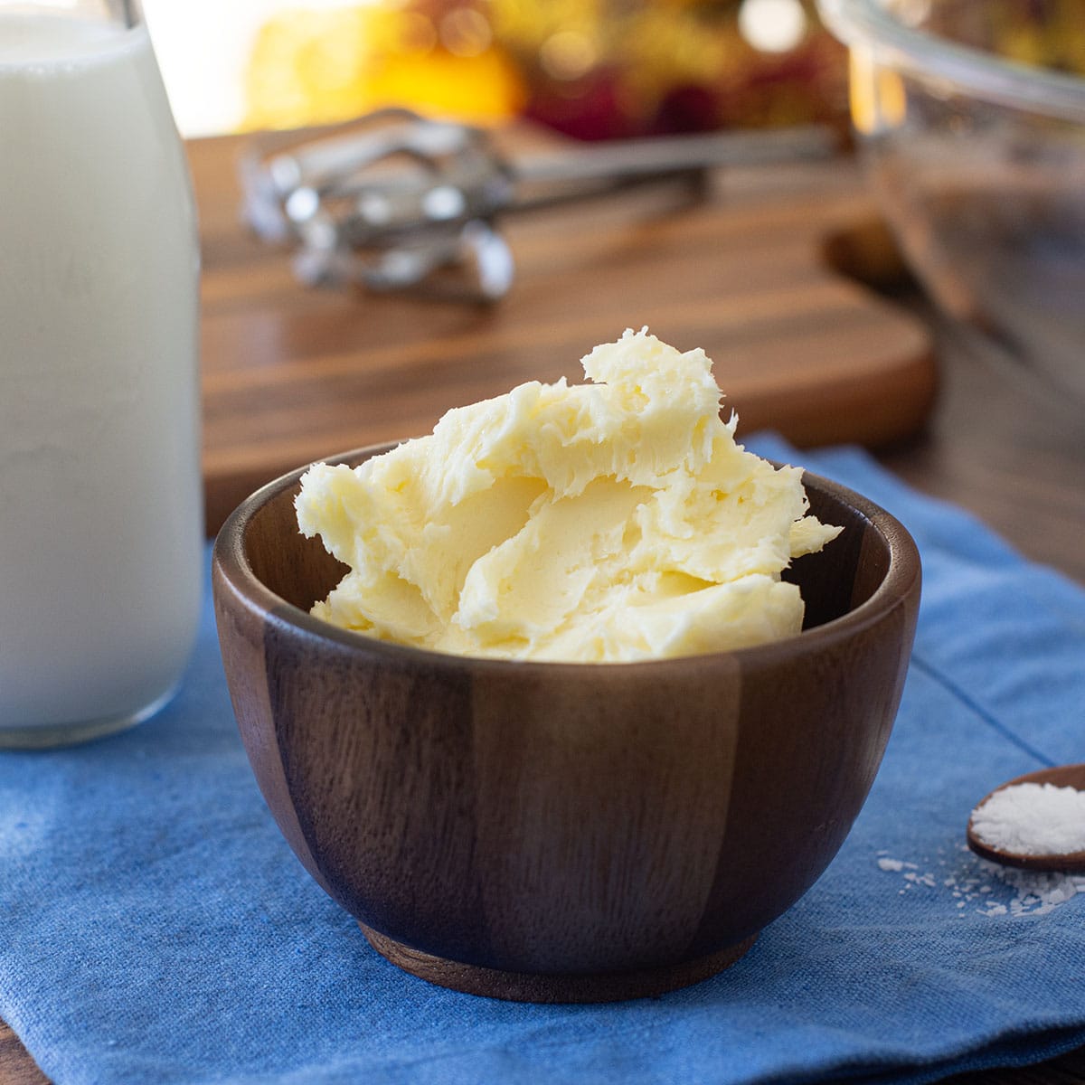 Wooden dish of homemade butter, spoon of salt, and glass jar of cream.