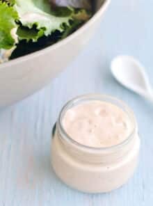 Glass jar of thousand island dressing with large bowl of salad greens in background.