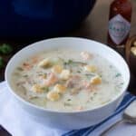 White bowl of salmon chowder with oyster crackers on top.