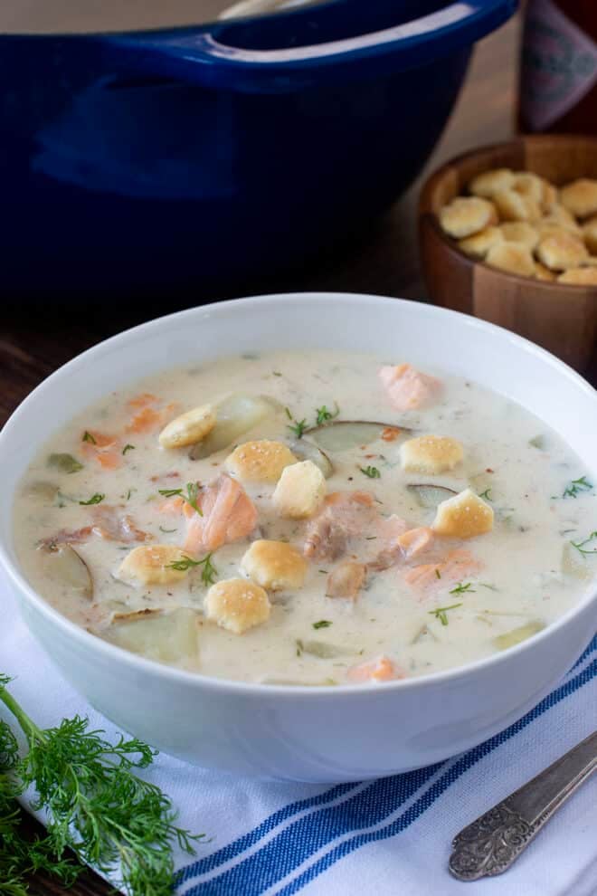 White bowl of salmon chowder with oyster crackers on top.