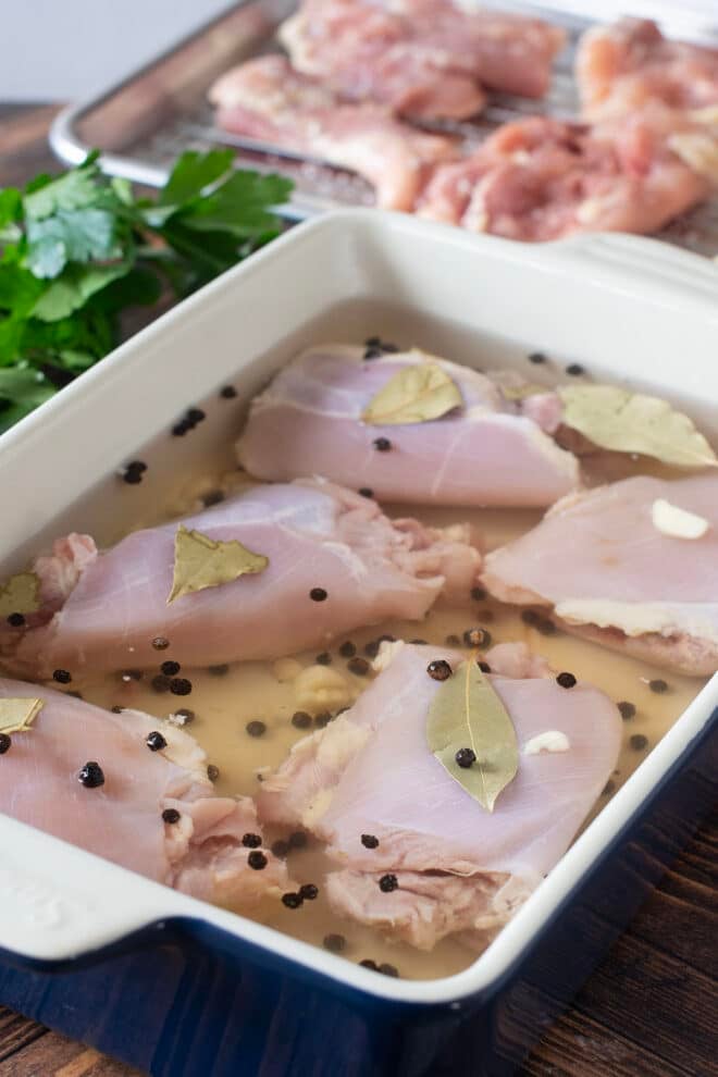 Chicken thighs brining in a white container with peppercorns and bay leaves.