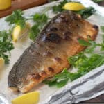Broiled side of salmon on a sheet pan lined with foil, with lemon wedges and parsley.