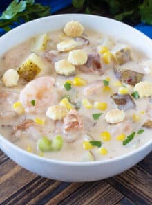 White bowl of shrimp chowder with potatoes and corn.