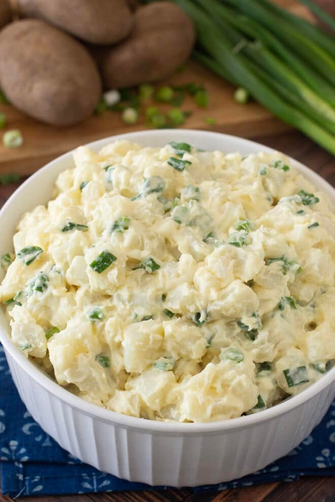 White round casserole dish with creamy potato salad with green onions.