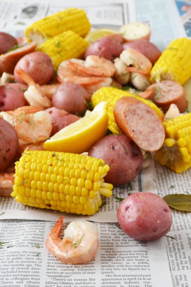 Corn on the cob, shrimp, red potatoes, sausage, and dill spread out on newspaper, all cooked and ready to eat.