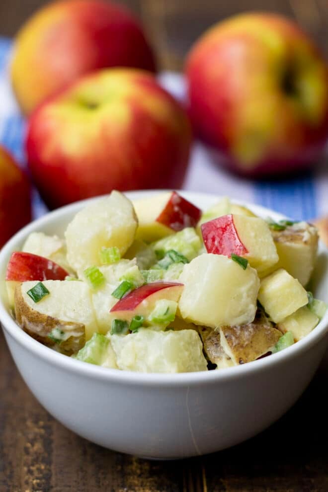 White bowl of potato salad with apples.