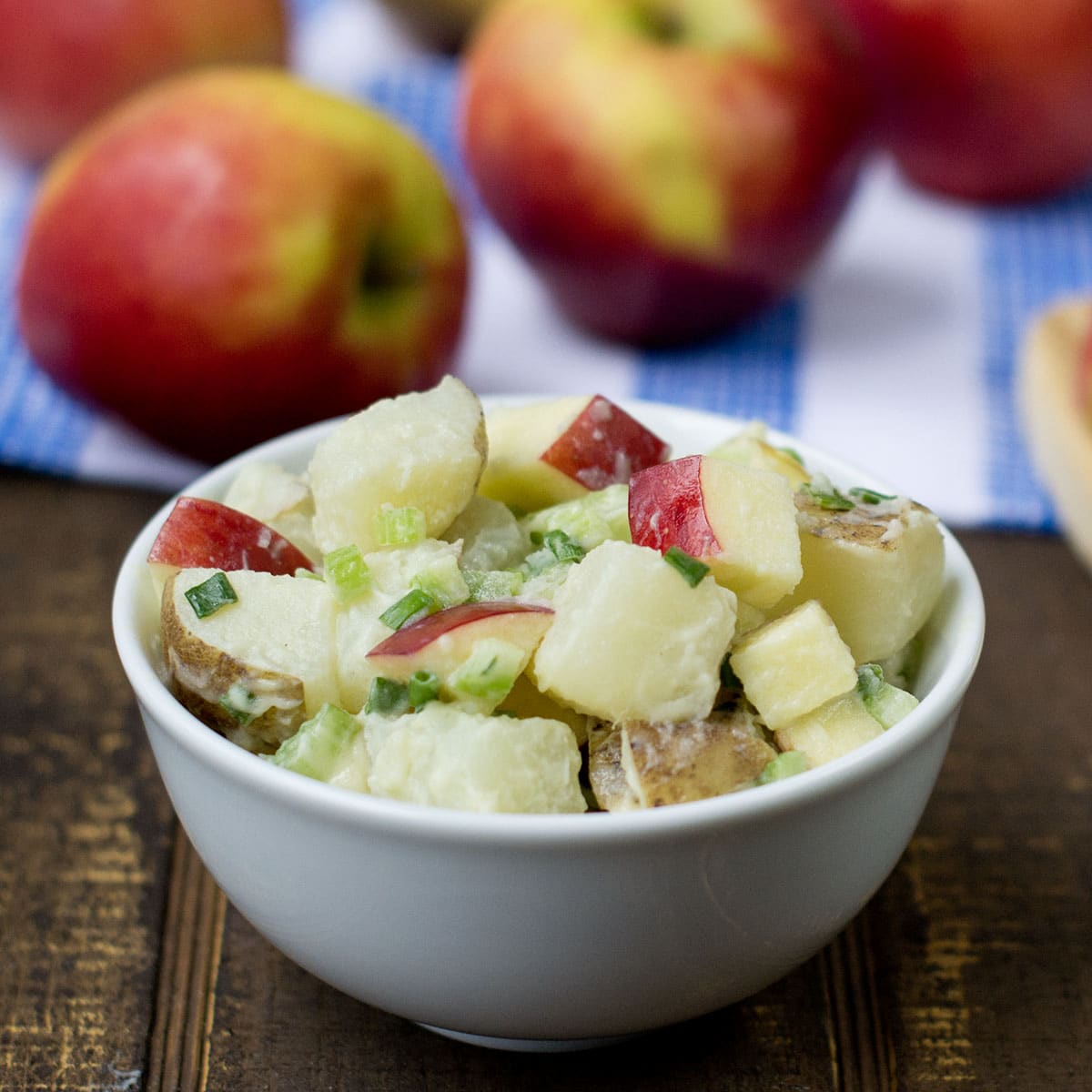 White bowl of potato salad with apples.