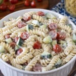 Round white serving dish with creamy pasta salad with cucumbers and tomatoes.