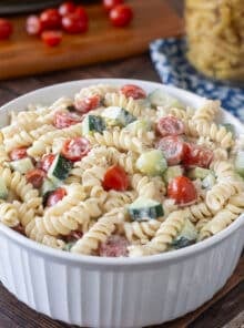 Round white serving dish with creamy pasta salad with cucumbers and tomatoes.