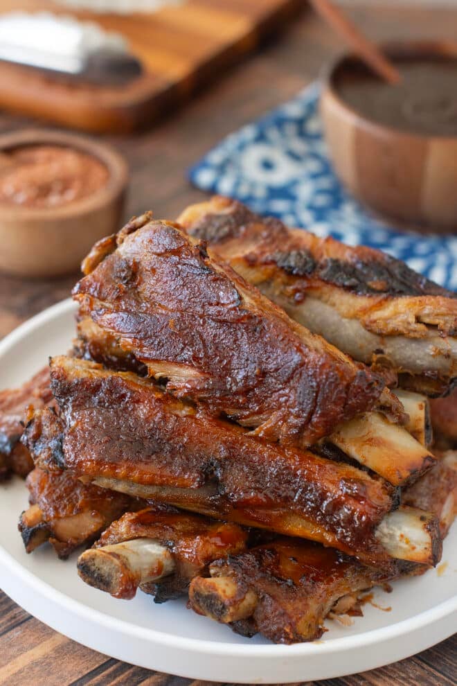Cooked St Louis ribs with BBQ sauce piled up on a white plate.