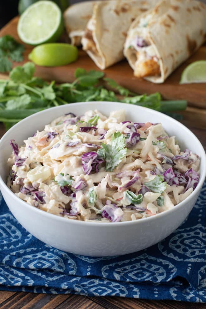 White serving bowl of creamy coleslaw with fish tacos in background.