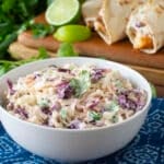 White serving bowl of creamy coleslaw with fish tacos in background.