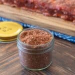 Glass jar with dry rub for ribs mixture, raw ribs in background.