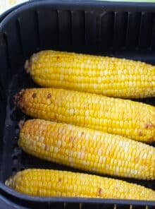 Four ears cooked corn in an air fryer basket.