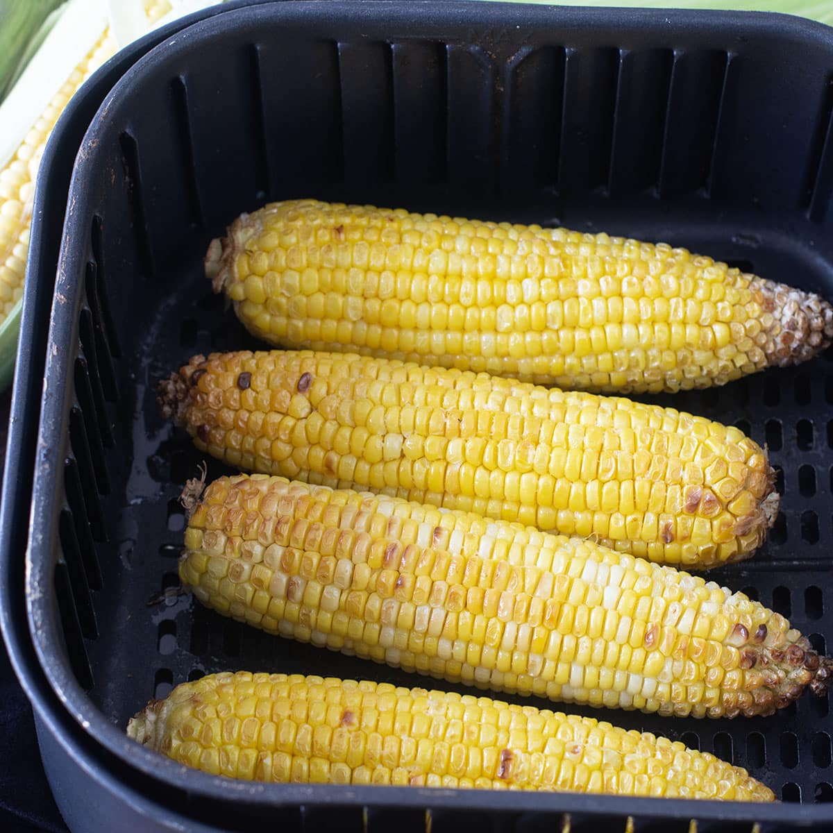 Four ears cooked corn in an air fryer basket.