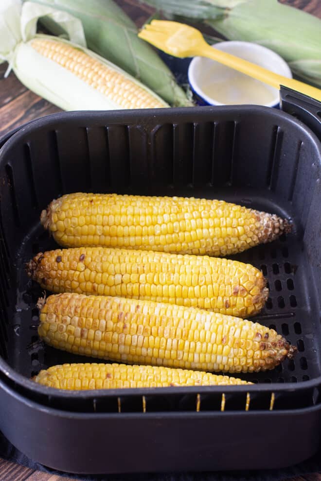 Four ears cooked corn in an air fryer basket.