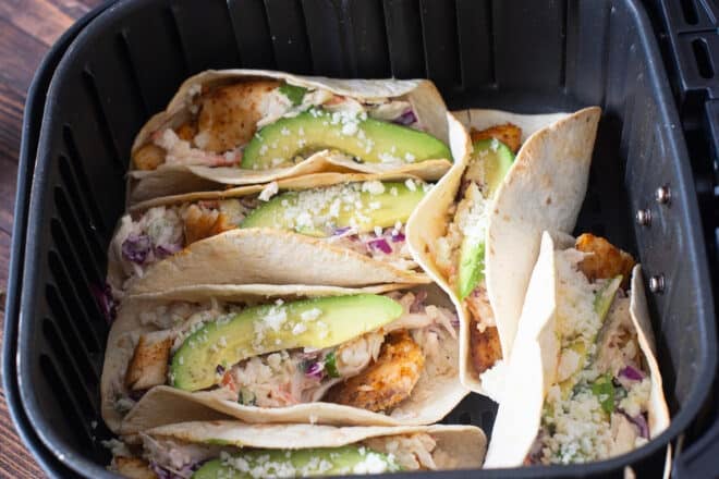 Fish tacos arranged in an air fryer basket, leaning against each other.