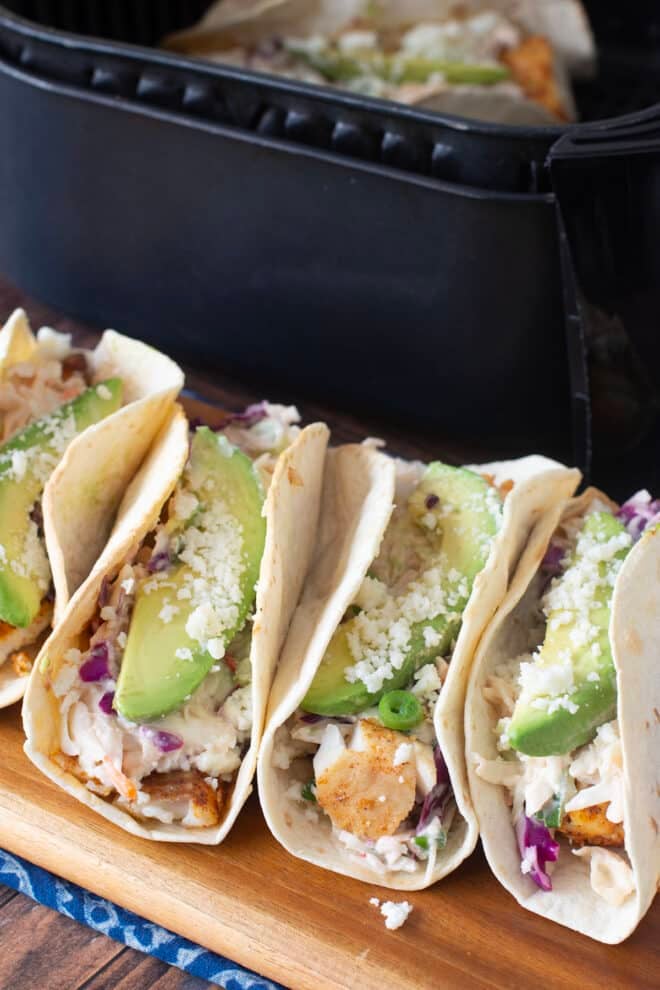 Tacos with flour tortillas, crispy fish, coleslaw, and avocado slices by air fryer basket.