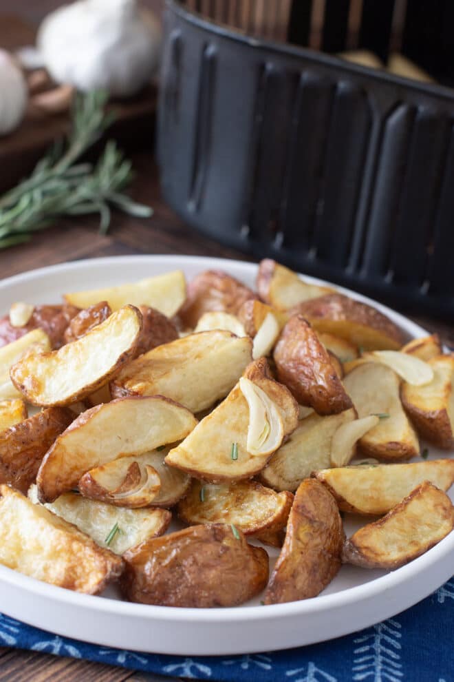 White plate of cooked red potatoes with garlic and rosemary in front of an air fryer.