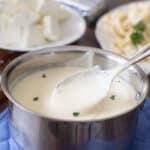 Cream cheese Alfredo sauce in a saucepan with pasta in the background.