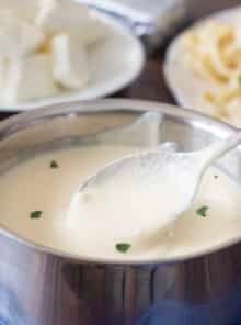 Cream cheese Alfredo sauce in a saucepan with pasta in the background.