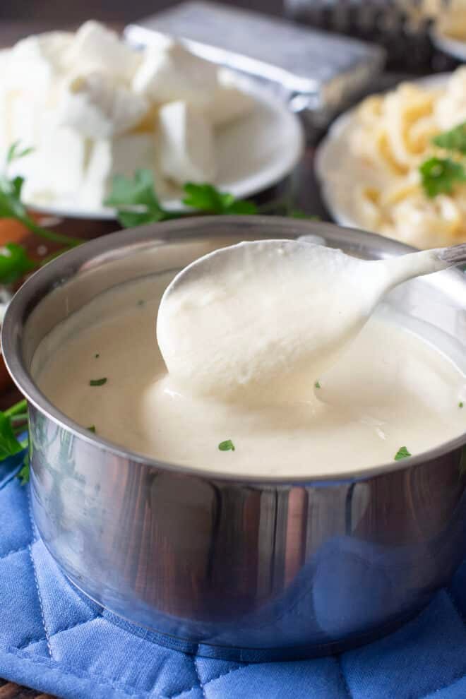 Cream cheese Alfredo sauce in a saucepan with pasta in the background.