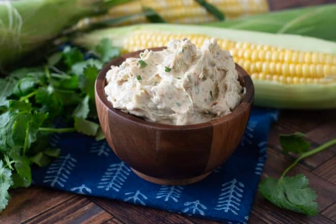 Small wooden bowl with compound butter, corn on the cob in background.