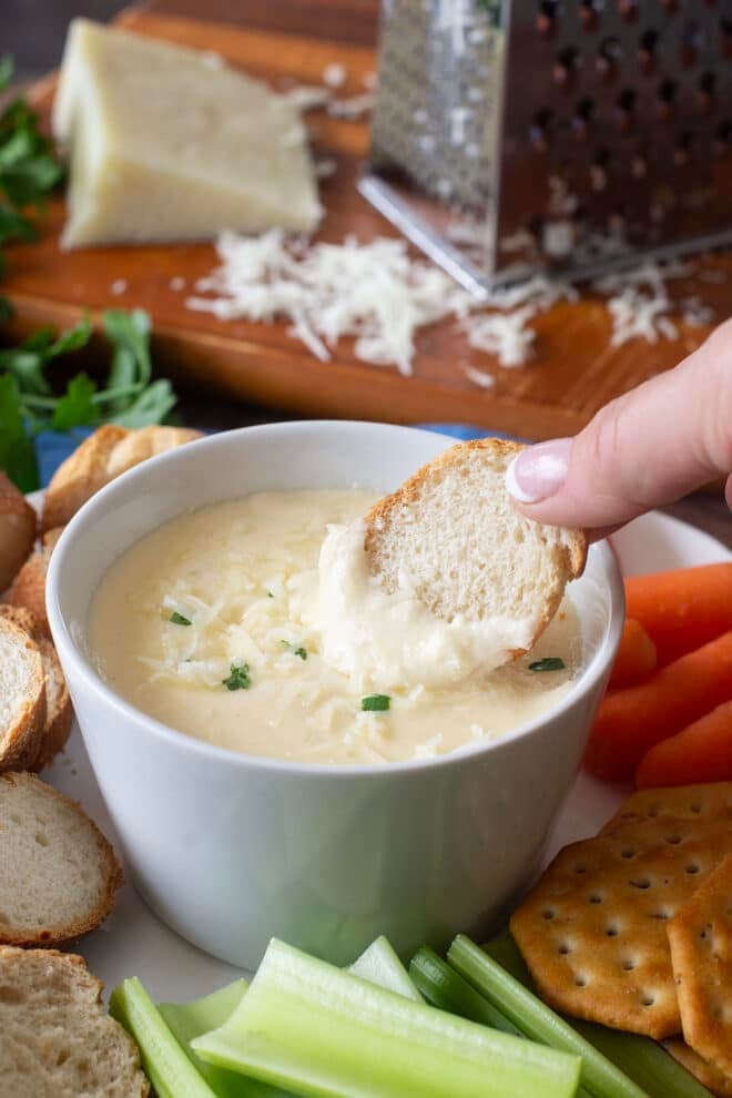 White bowl of parmesan cream cheese dip with cracker.