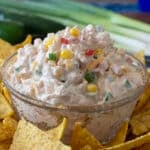 Glass bowl of cheesy creamy corn dip surrounded by tortilla chips.