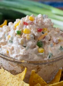 Glass bowl of cheesy creamy corn dip surrounded by tortilla chips.