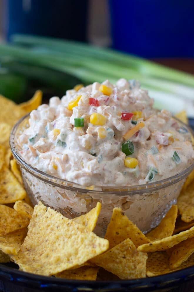 Glass bowl of cheesy creamy corn dip surrounded by tortilla chips.