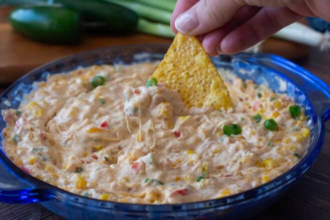 Hot cheesy corn dip in blue bowl with tortilla chip dipping.