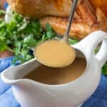 White gravy boat with turkey gravy, roast turkey in background.