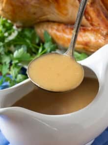 White gravy boat with turkey gravy, roast turkey in background.