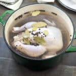 Large pot with raw chicken in a brine with bay leaves and peppercorns.