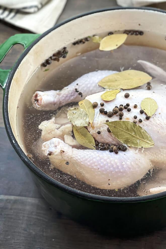 Large pot with raw chicken in a brine with bay leaves and peppercorns.