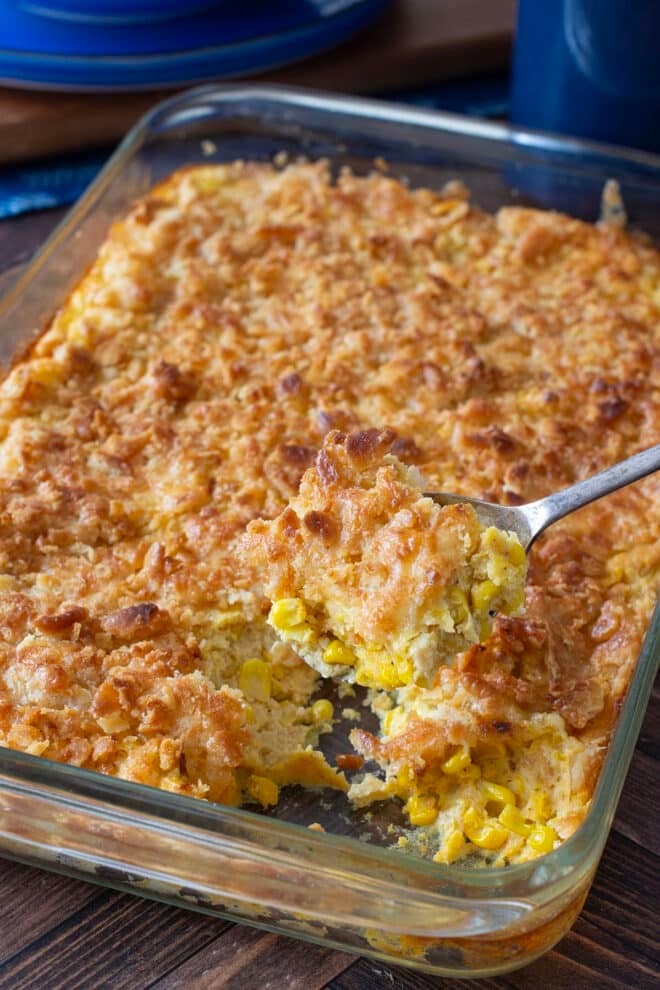 Glass casserole dish of scalloped corn with browned crunchy topping.