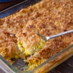 Glass casserole dish of scalloped corn with browned crunchy topping.